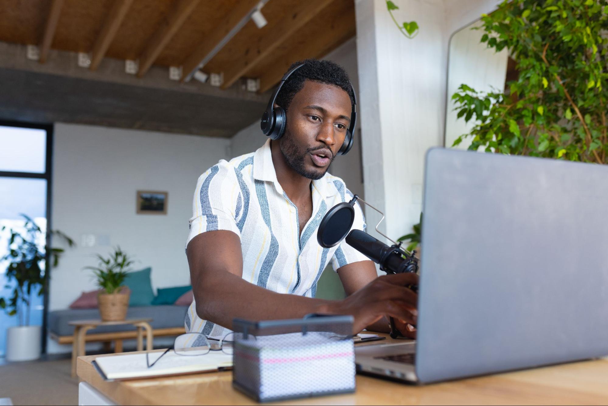 African-American man, with headphones and a microphone, typing. 