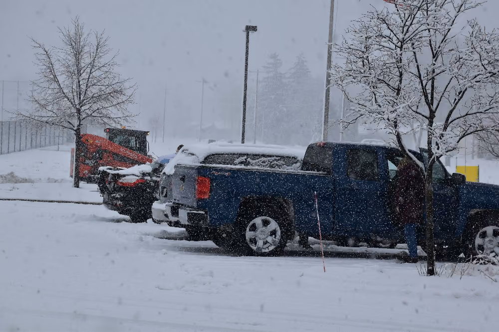 Snow-covered pickup trucks in a parking lot during snowfall.