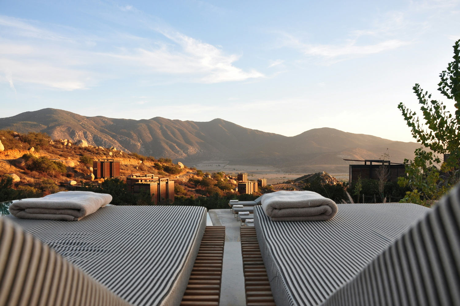 Two sun loungers on top of a wooden deck overlooking the mountains.