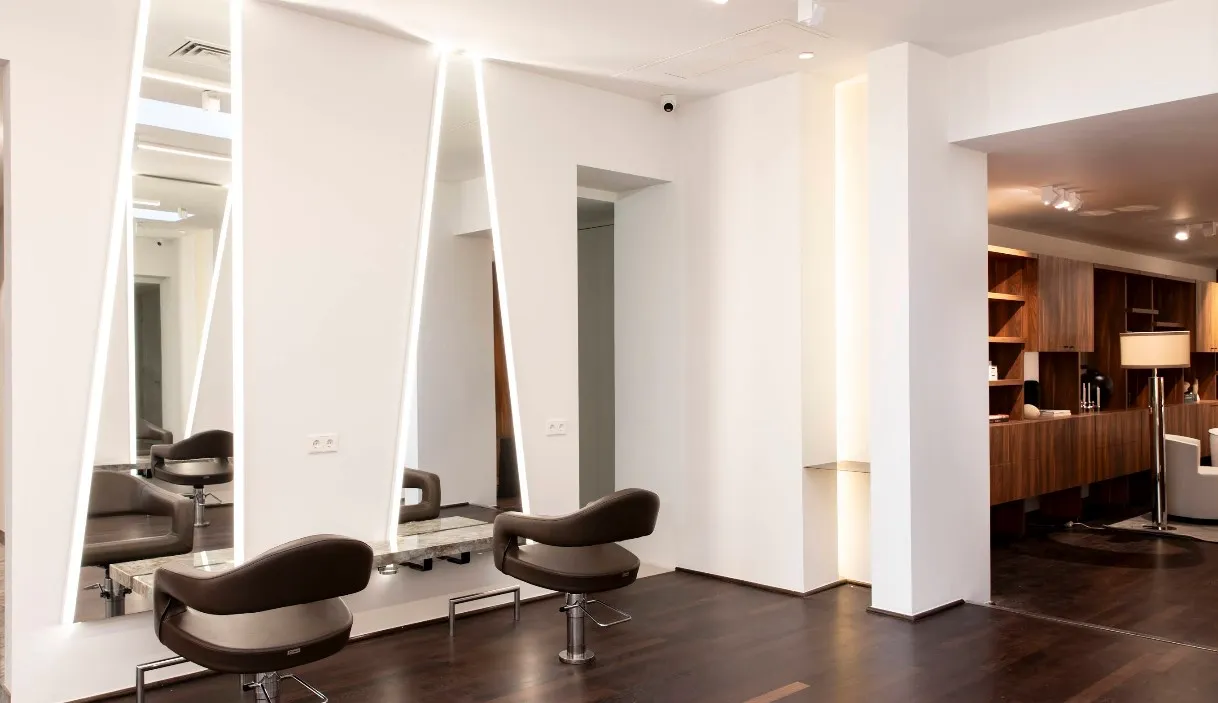 Люксова рецепція салону Daniel Galvin у Selfridges, Лондон: дзеркальні стіни з золотими акцентами, бежевий диван, полиці з косметикою та шампанським на мармуровому барі — шопінг-атмосфера для преміум-стрижок.