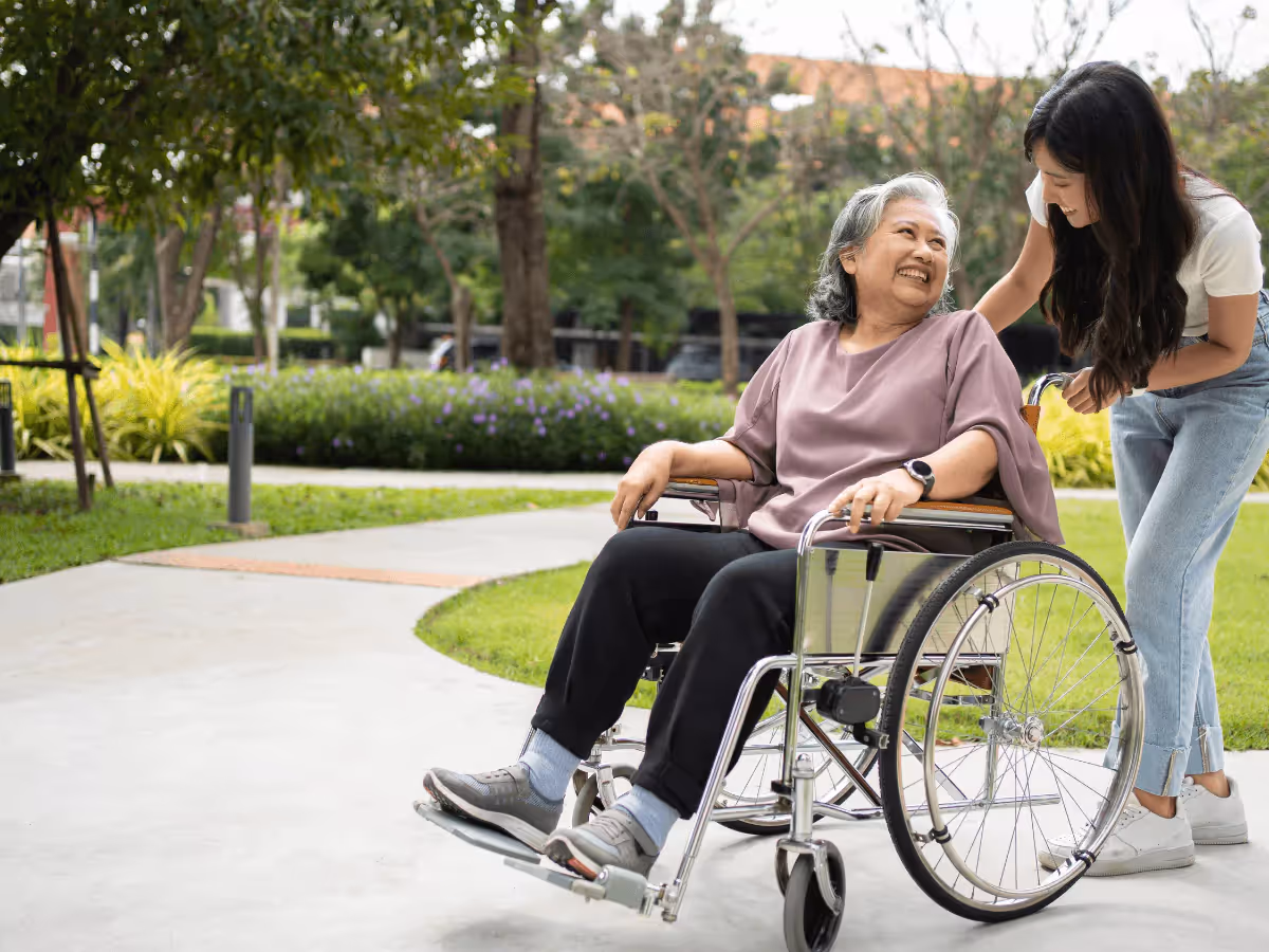 A caregiver assisting a smiling elderly woman in a wheelchair outside, illustrating the importance of proper in-home care and strategies for managing summer heat for seniors.