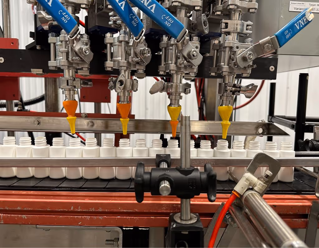 Automated liquid filling equipment precisely dispensing supplement formulas into plastic bottles during nutraceutical manufacturing | Steuart Nutrition