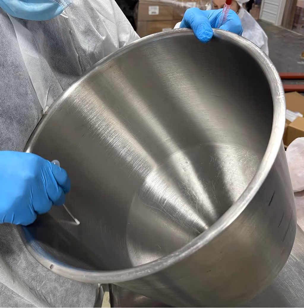 Technician wearing gloves inspecting stainless steel blending container for supplement formulation quality control | Steuart Nutrition