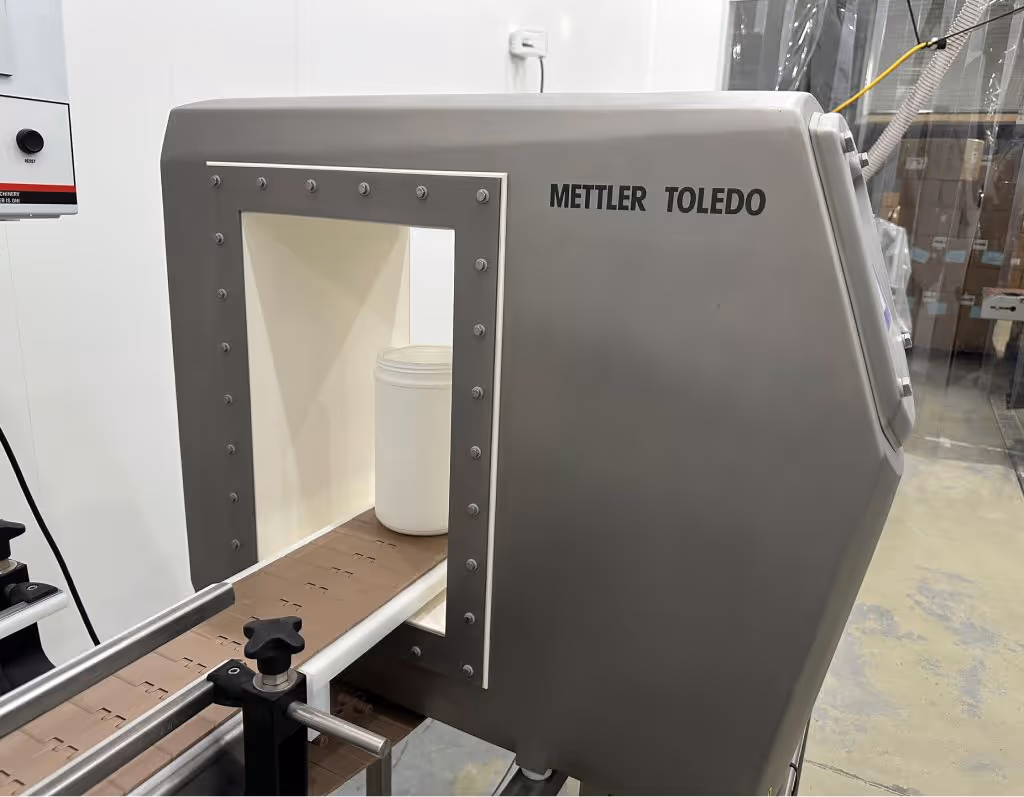 Mettler Toledo industrial metal detection system ensuring safety and quality control by scanning sealed supplement containers on automated packaging line | Steuart Nutrition