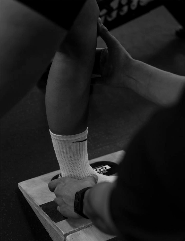 A coach checking a client's ankle and knee position on a slant board