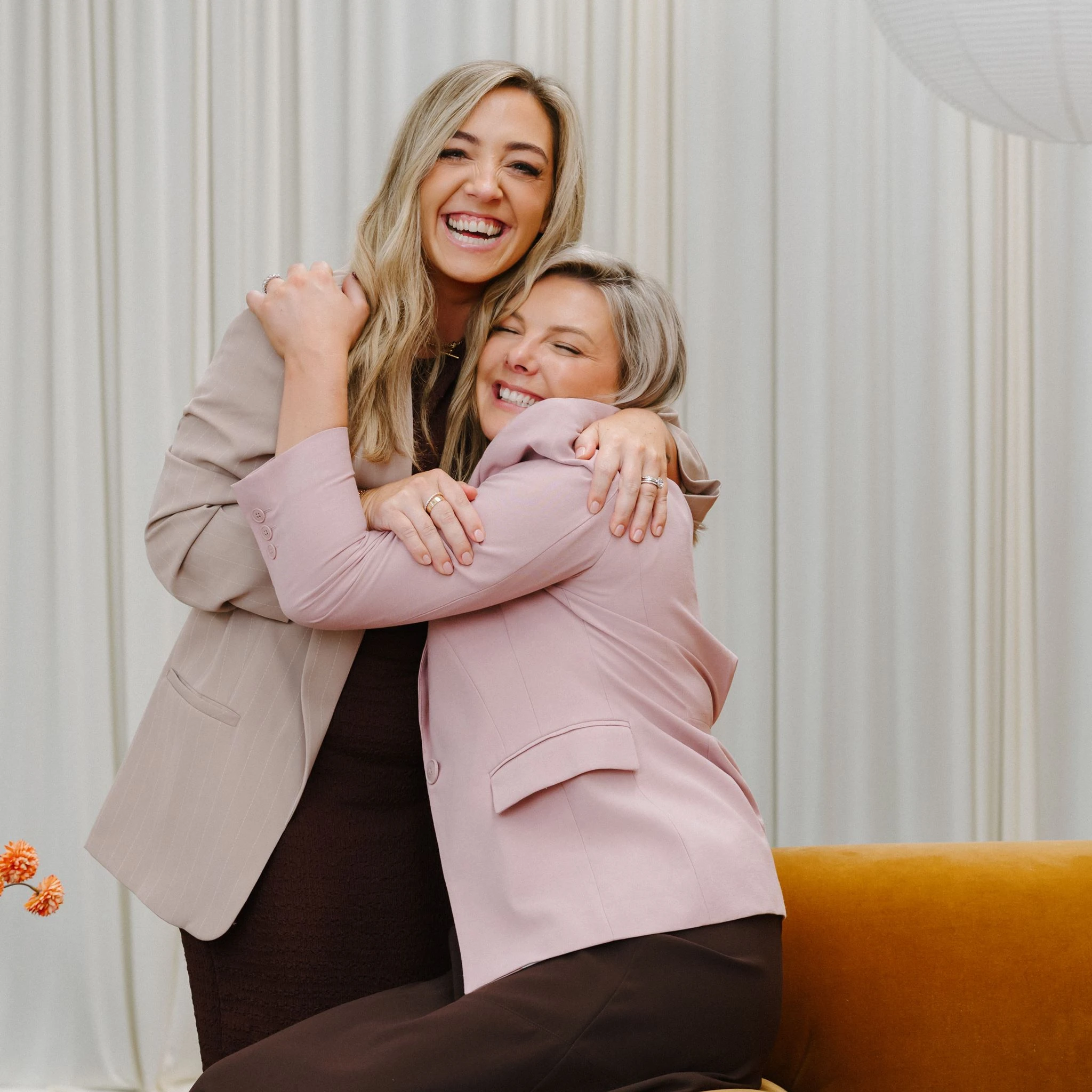 Two woman in suit jackets embracing one another
