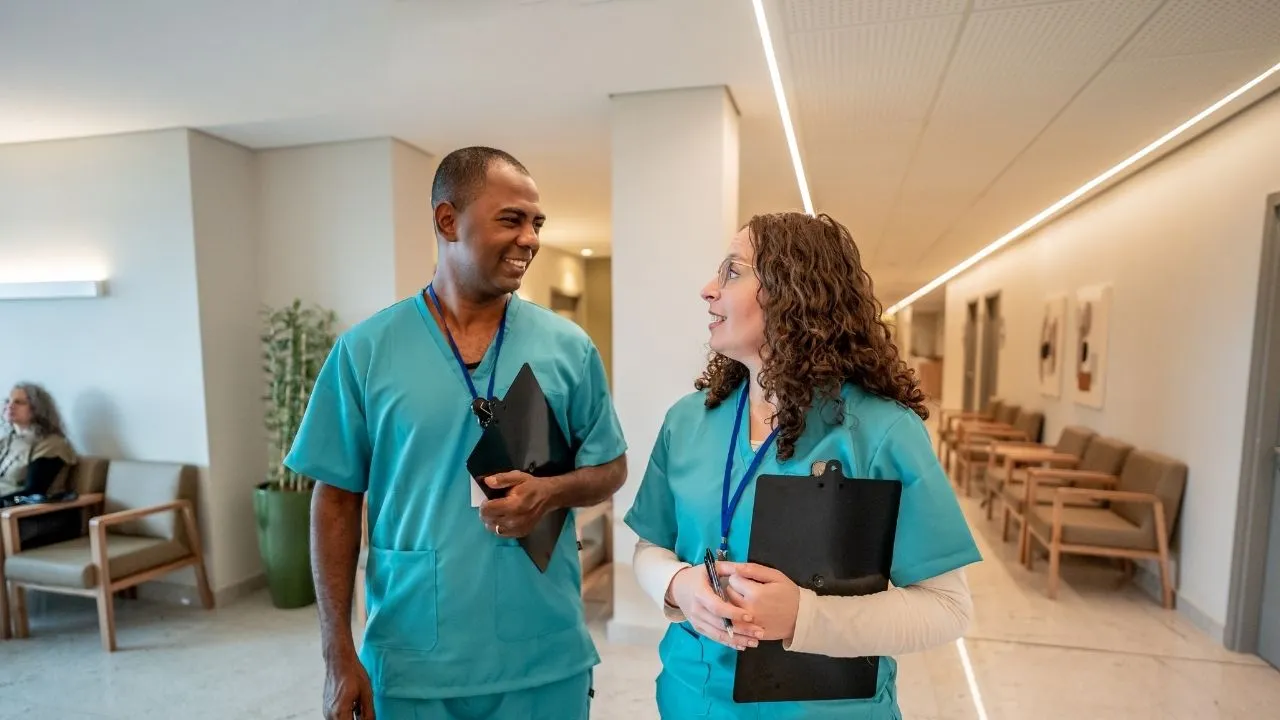 Two nurses speaking to each other as they walk down a hallway