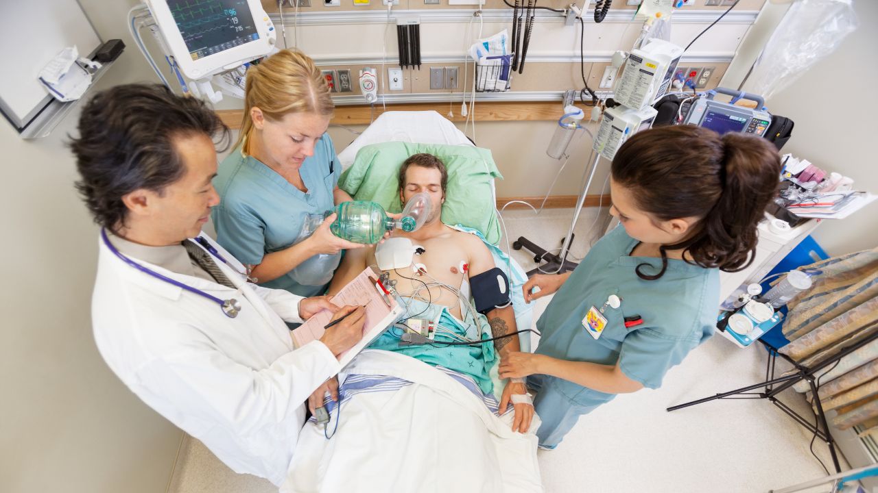 Medical team in a hospital room providing respiratory support to a male patient on a hospital bed