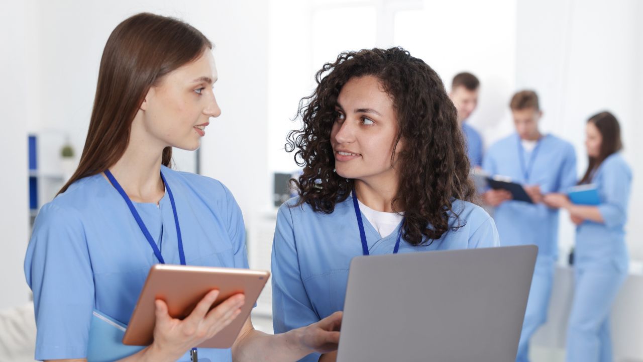 A nurse speaking with another nurse with laptop and notes