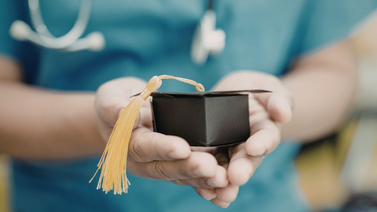 Nurse in scrubs holding a small graduation cap in their hands