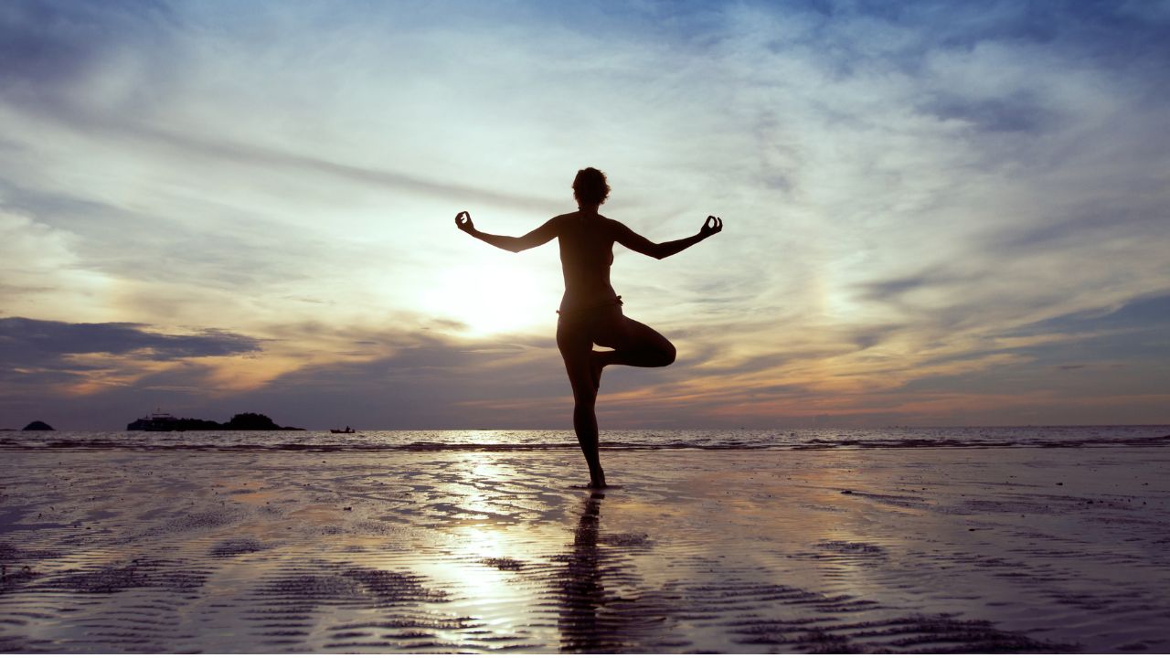 Person practicing yoga on a beach at sunset