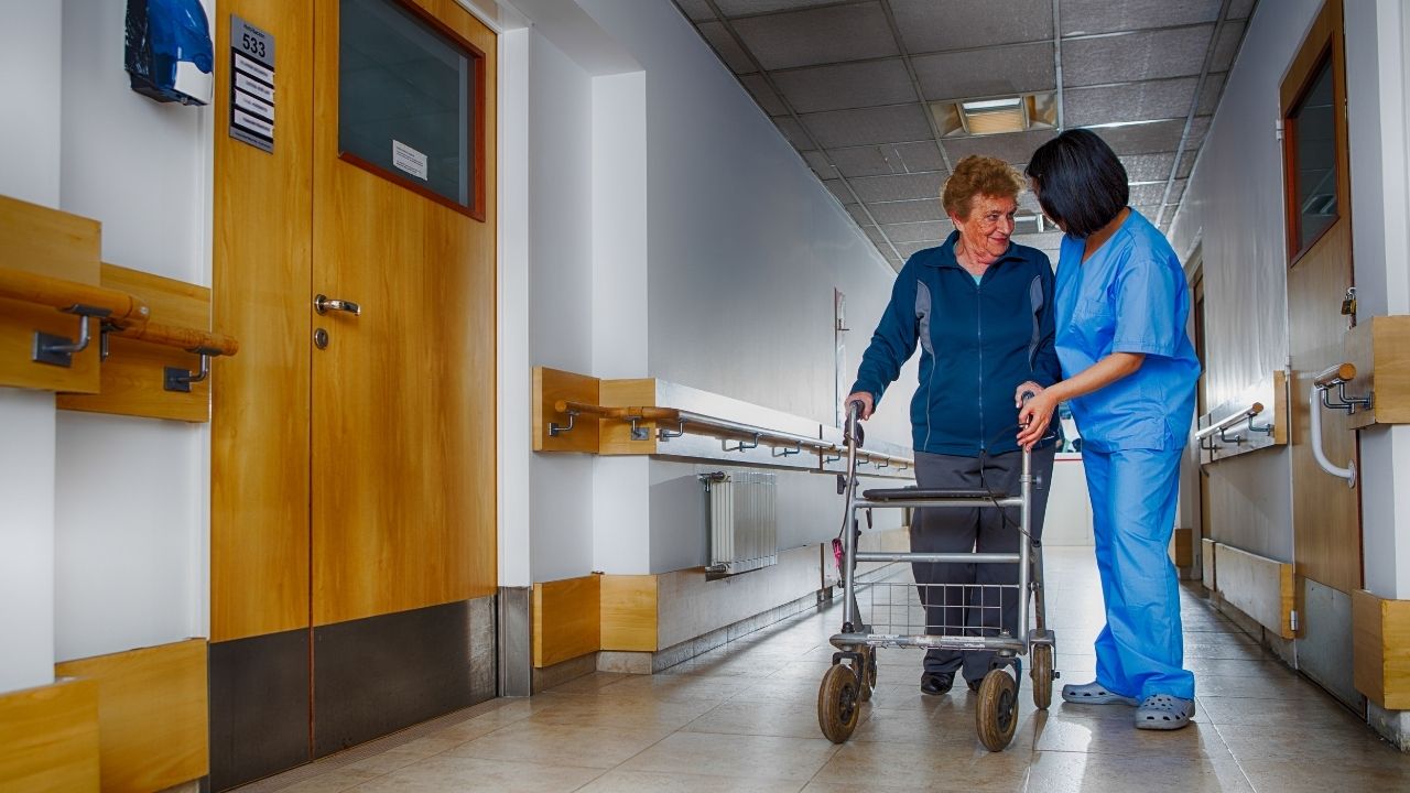 Nurse assisting an older adult using a walker in a hallway