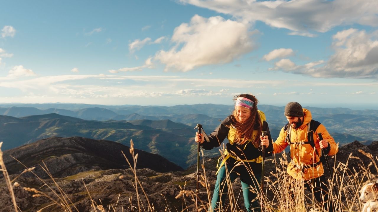 Couple hiking with trekking poles and dog on a mountain ridge.