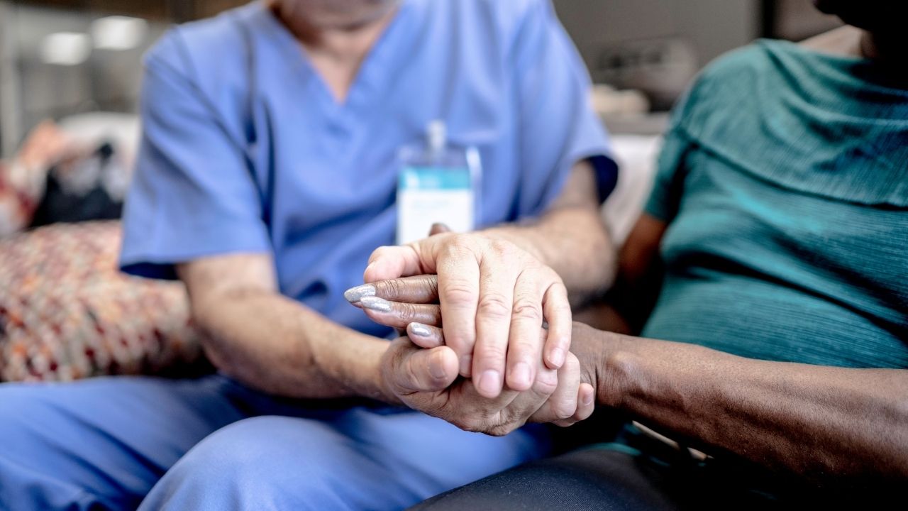 Nurse holding hands with a seated patient in a room