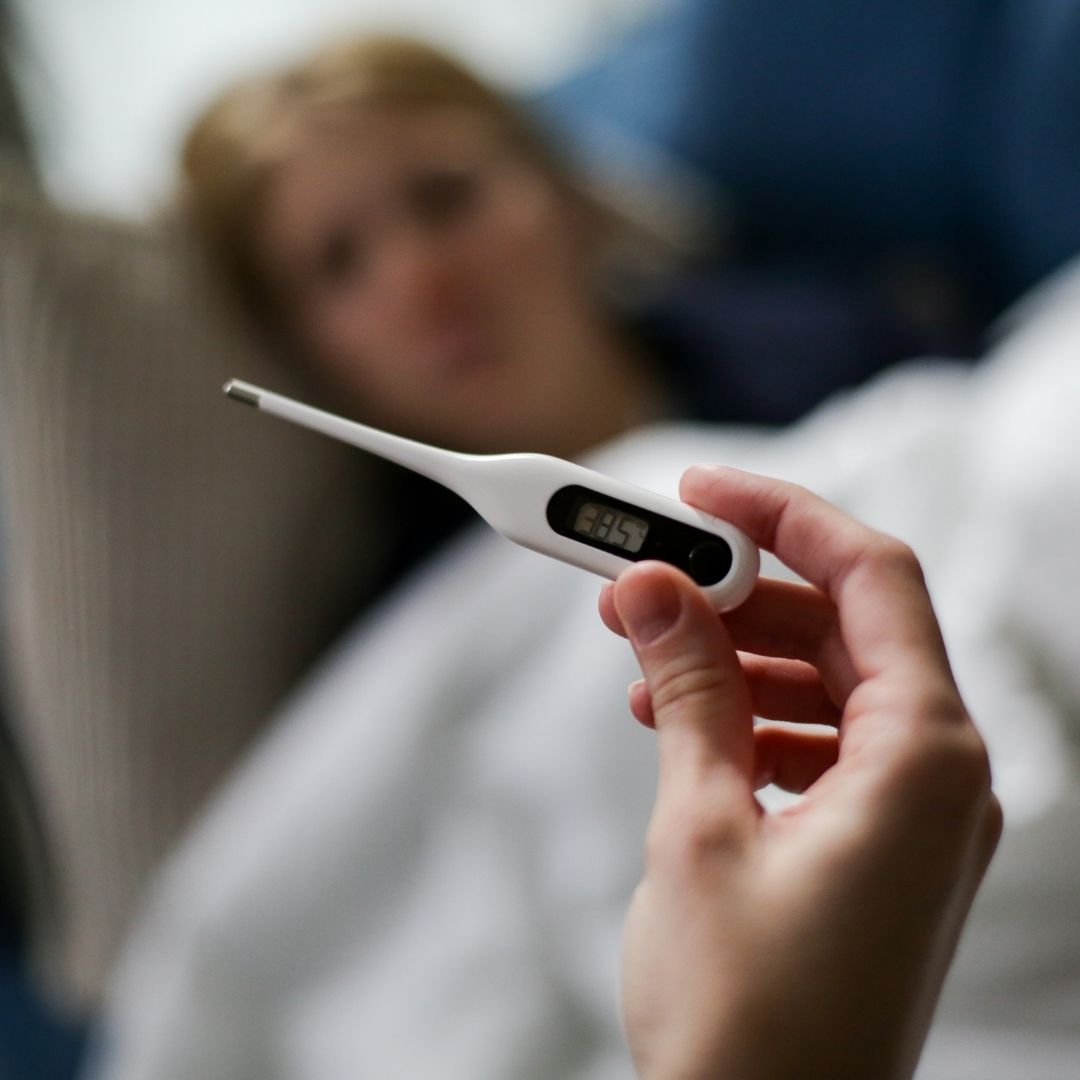 A nurse holding a thermometer and a patient in the background