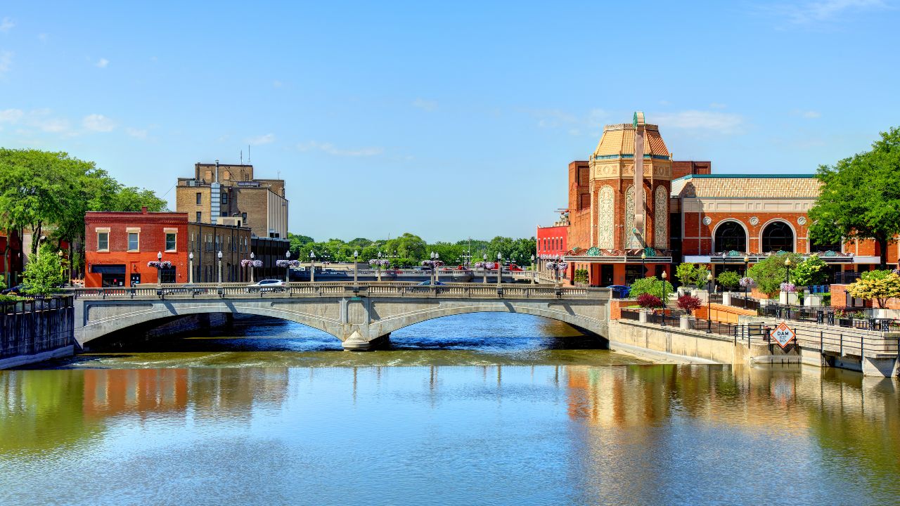 a view of a cityscape with brick buildings, tower, arched bridge over river