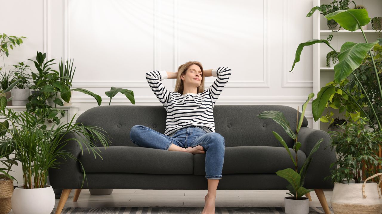 a woman relaxing on a couch surrounded by house plants