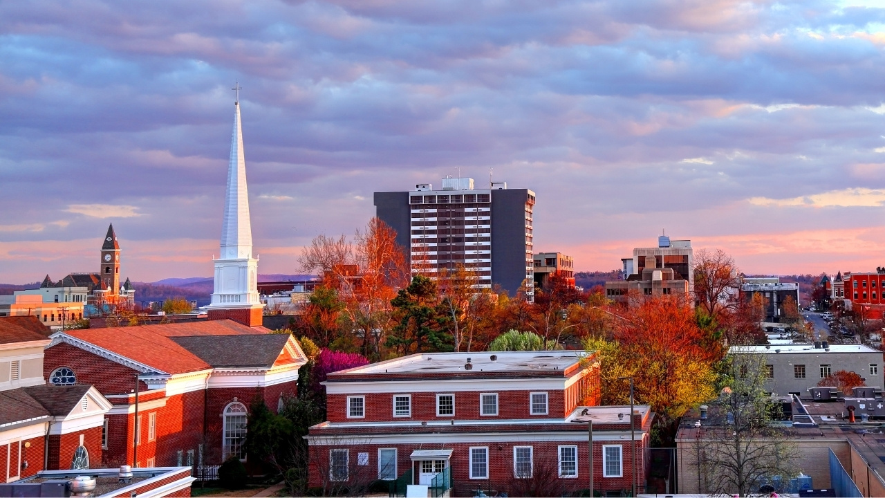 cityscape of Fayetteville Arkansas with red brick buildings, trees, and a tall church steeple under a cloudy sky