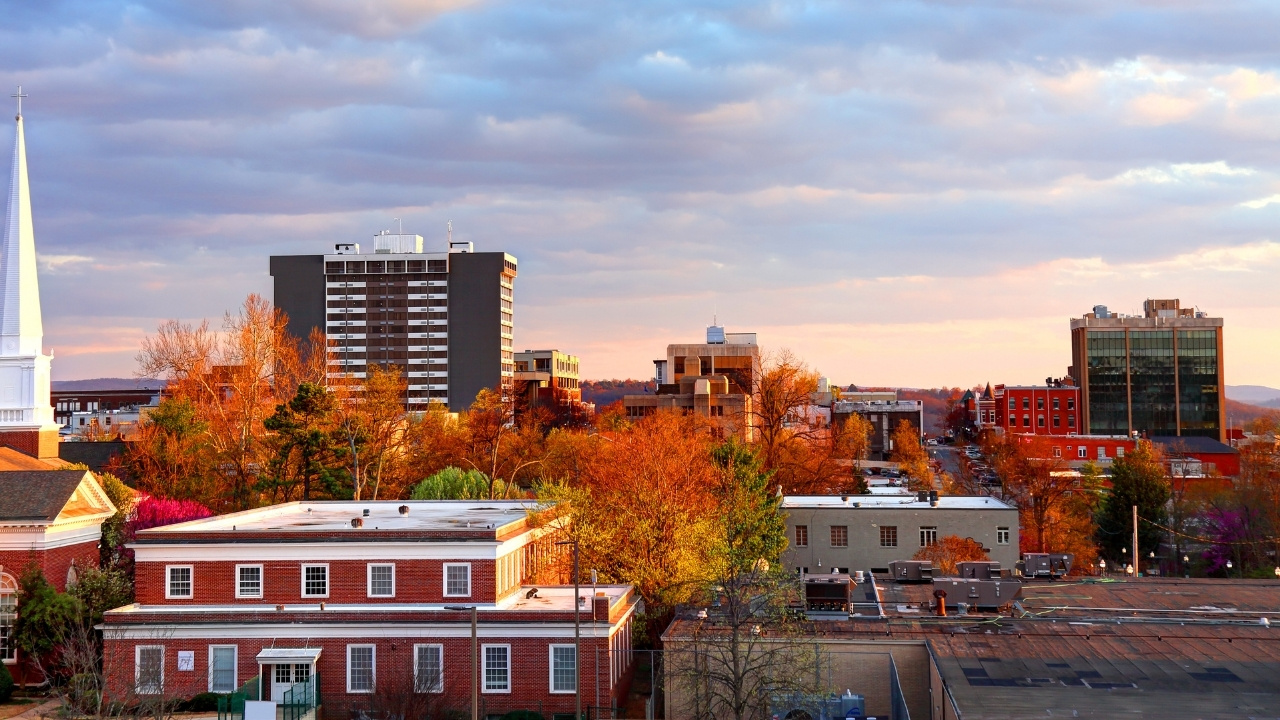 cityscape of Fayetteville Arkansas with red brick buildings, trees, and a tall church steeple under a cloudy sky