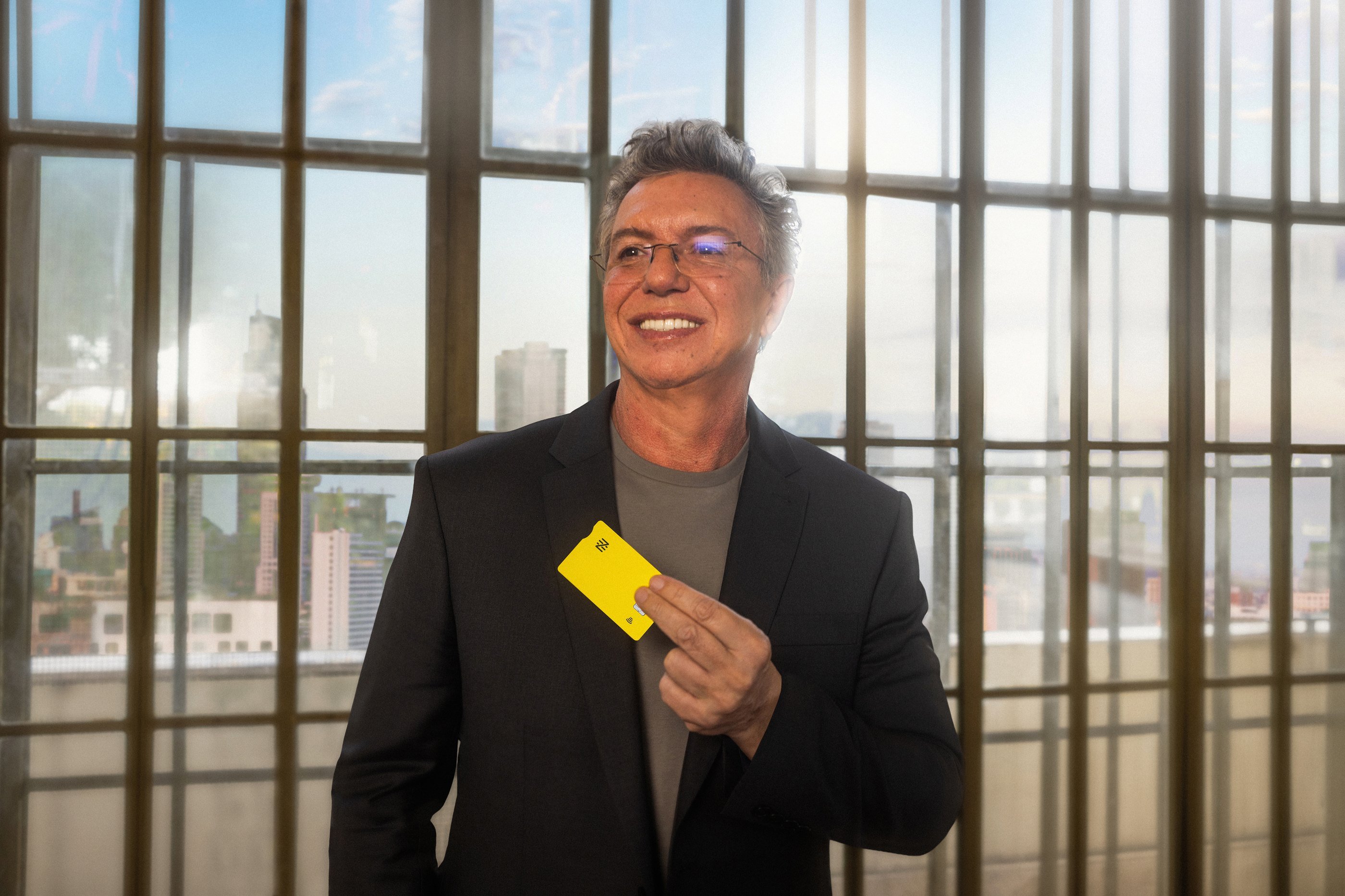 Homem sorrindo segura um cartão Nomad amarelo