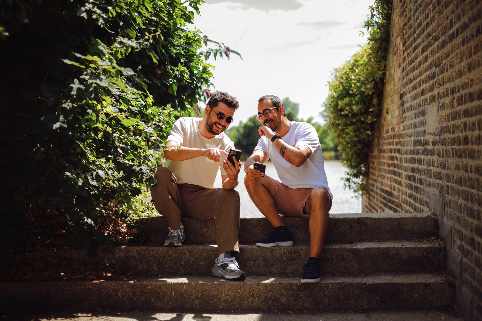 Dois amigos sentados em uma escadaria olhando o celular durante uma viagem