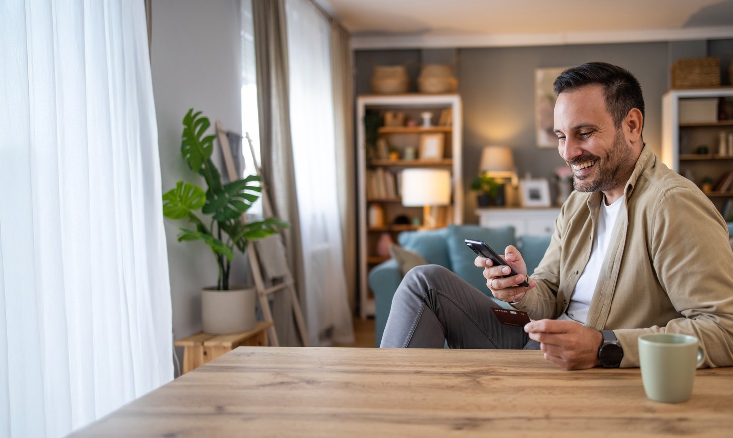 Homem sorrindo enquanto usa o celular em casa