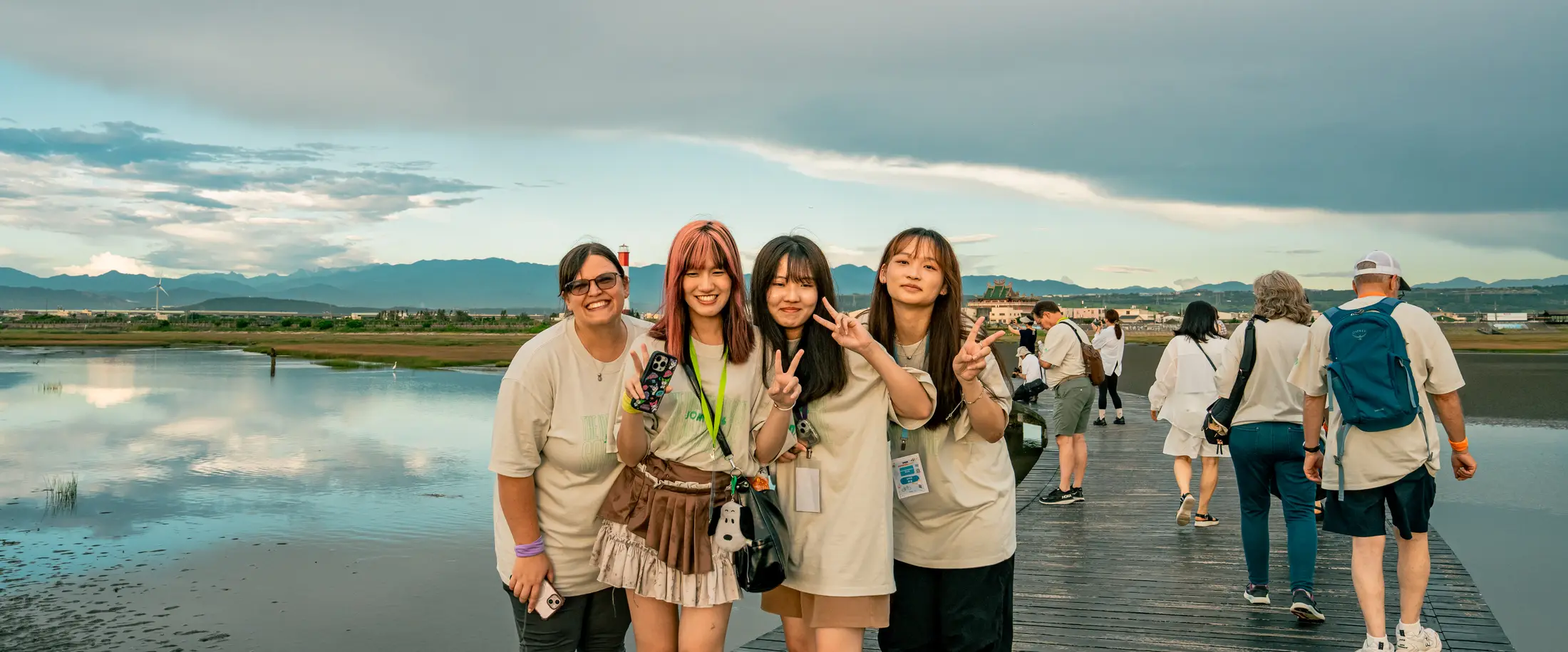 Students from Taichung International Fellowship smiling on the boardwalk at Gaomei Wetlands, with Taiwan's mountains behind them