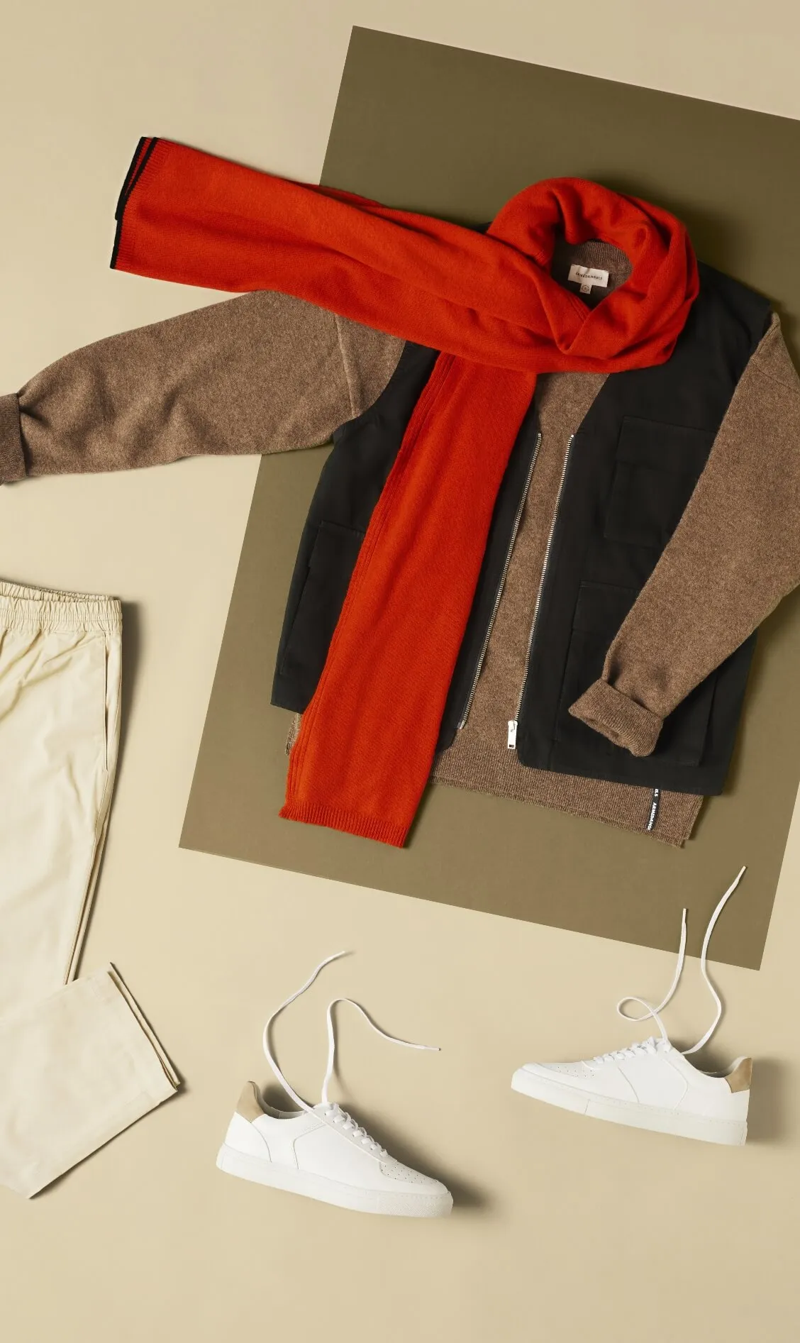 An image of a red scarf, an autumn jacket, cream colored pants and white sneakers taken from bird's eye view