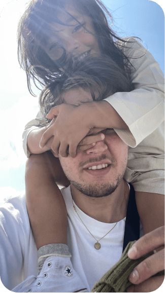 An image of a little girl standing on top of her father's head, covering his eyes