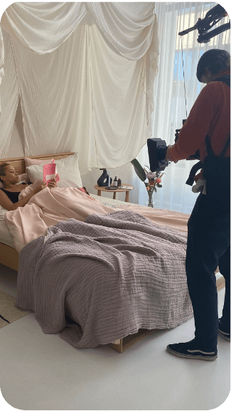 An image of a photographer taking a photo of a woman laying in bed and reading a book