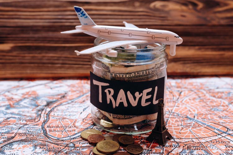 A plastic toy plane placed on top of a small glass jar, labelled "travel", filled with notes and coins. Both items are placed on a spread out map of a city.