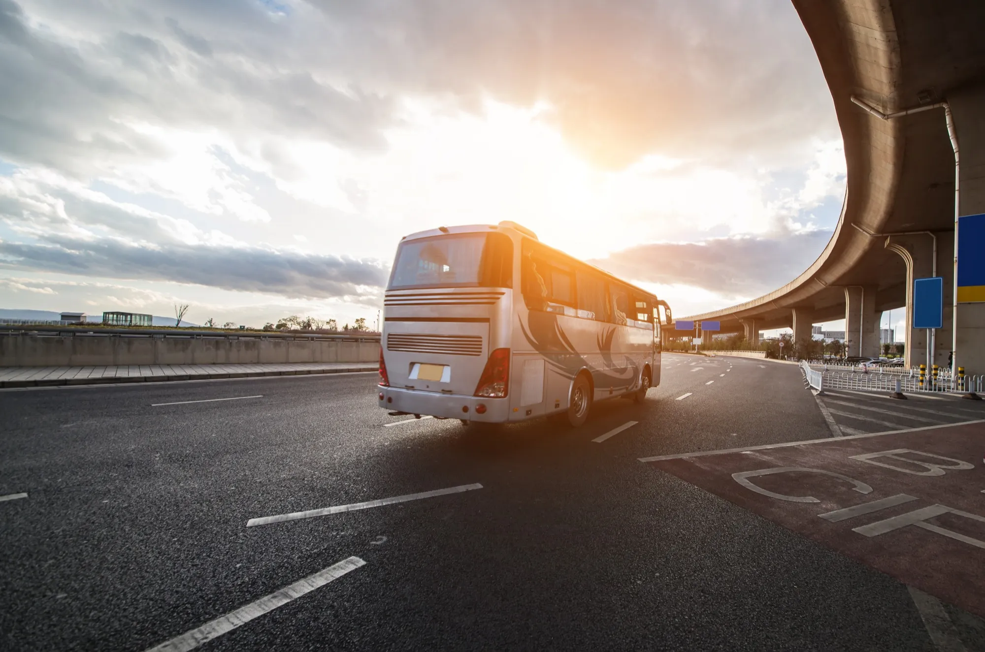 A white bus driving down a highway next to a bridge.