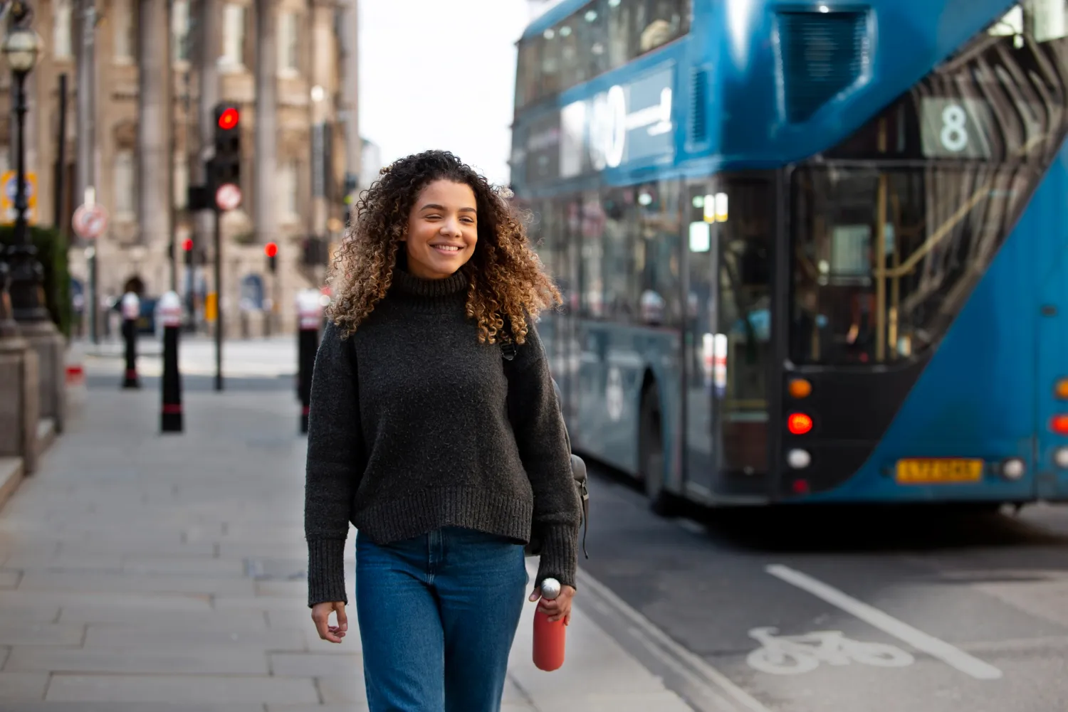 A woman walking down the street in front of a double decker bus.