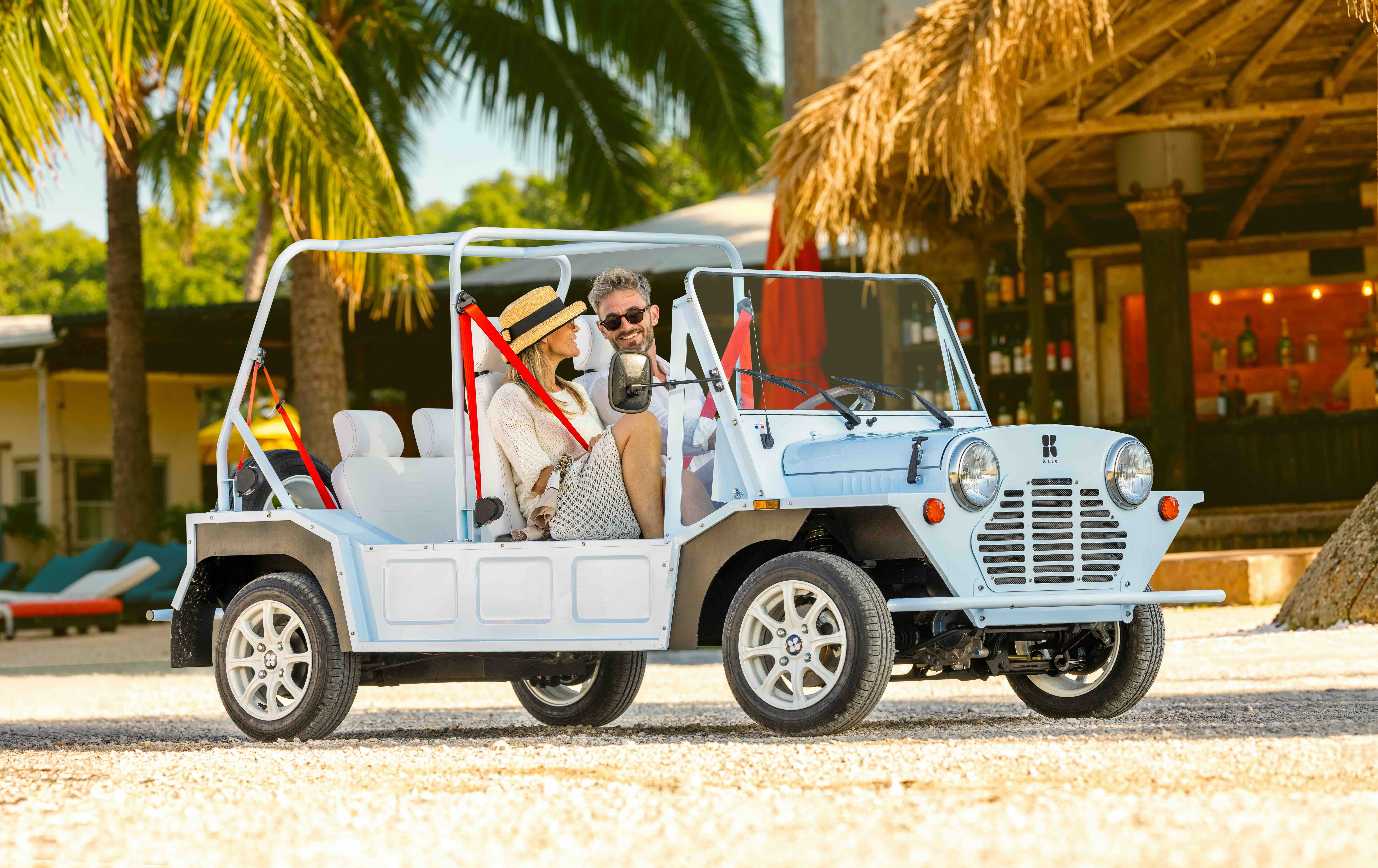 Voitures de plage anciennes, dont Mini Moke, Citroën Méhari, Fiat 500 Jolly et Kate électrique, garées au bord de la mer.