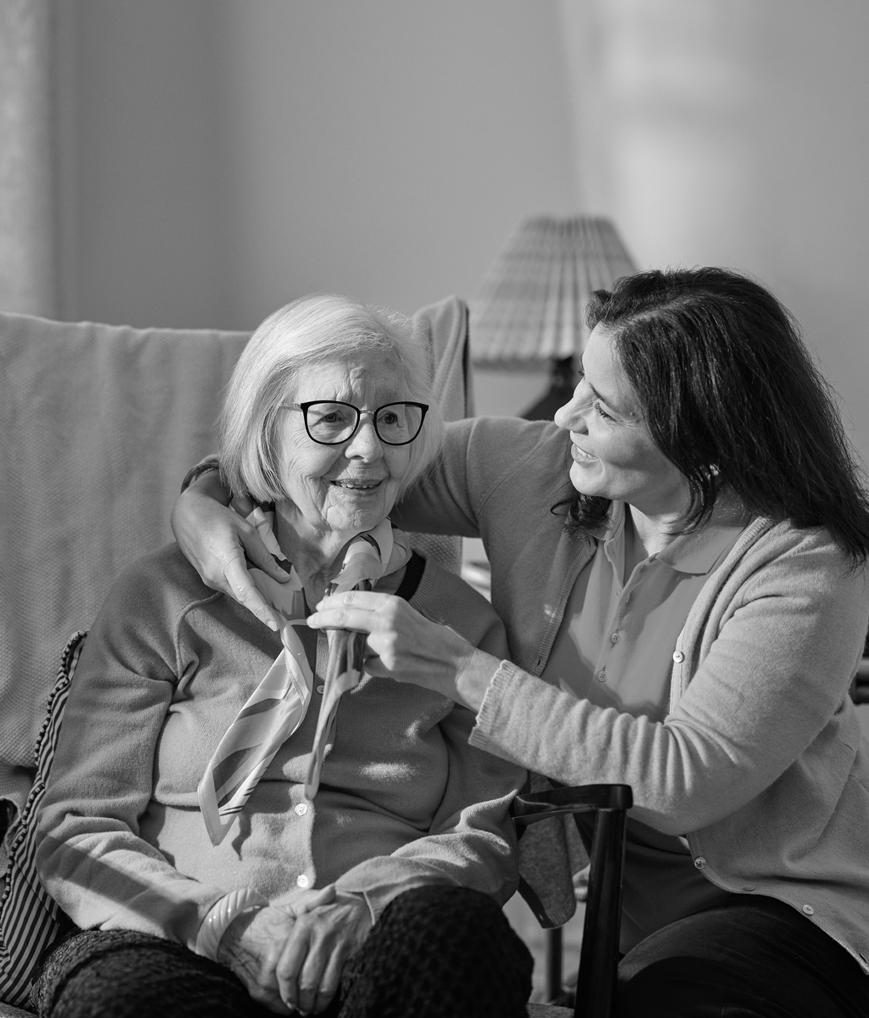 A caregive engages in conversation with an older woman, both smiling and sharing a warm moment together.