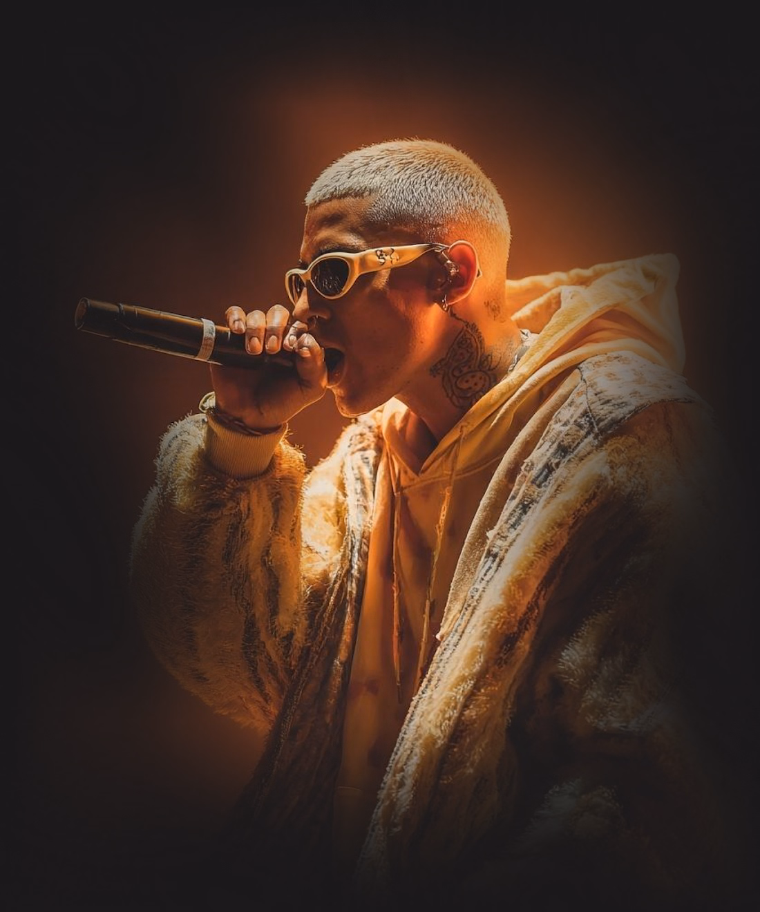 A cool rapper on stage holding a microphone surrounded by warm orange lights