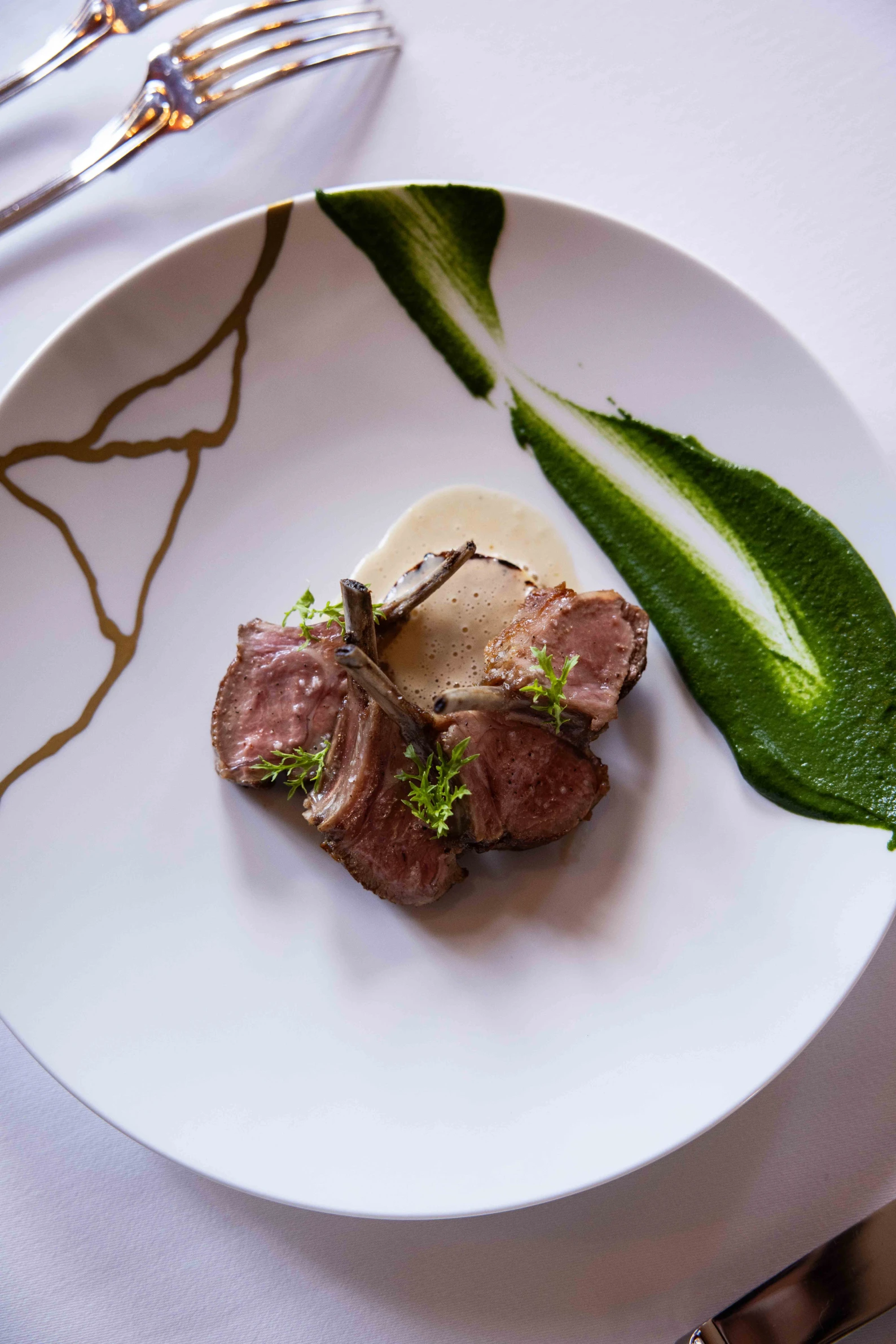 Côtes d'agneau grillées servies avec une sauce verte étalée et une sauce crémeuse au centre de l'assiette, garnies de petites feuilles vertes.
