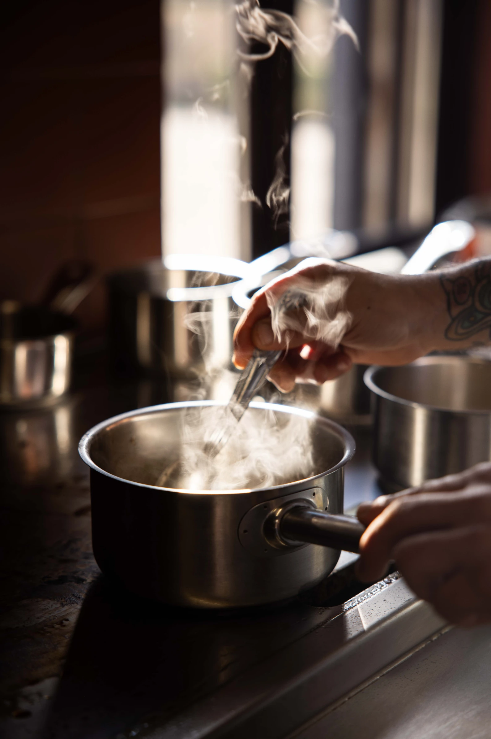 Main cuisinier remuant une casserole fumante sur une cuisinière dans une cuisine.