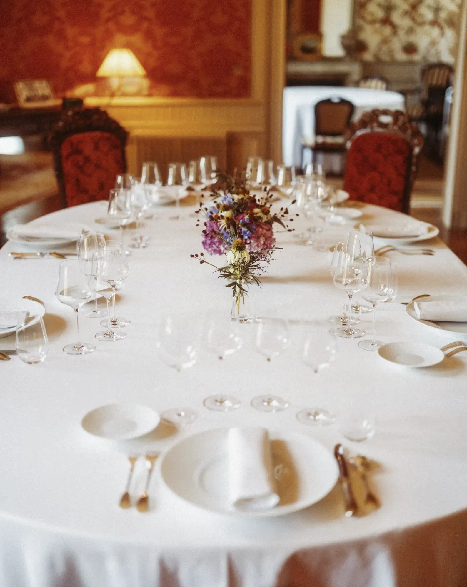 Table élégamment dressée avec nappe blanche, verres à vin, couverts et bouquet de fleurs colorées au centre.
