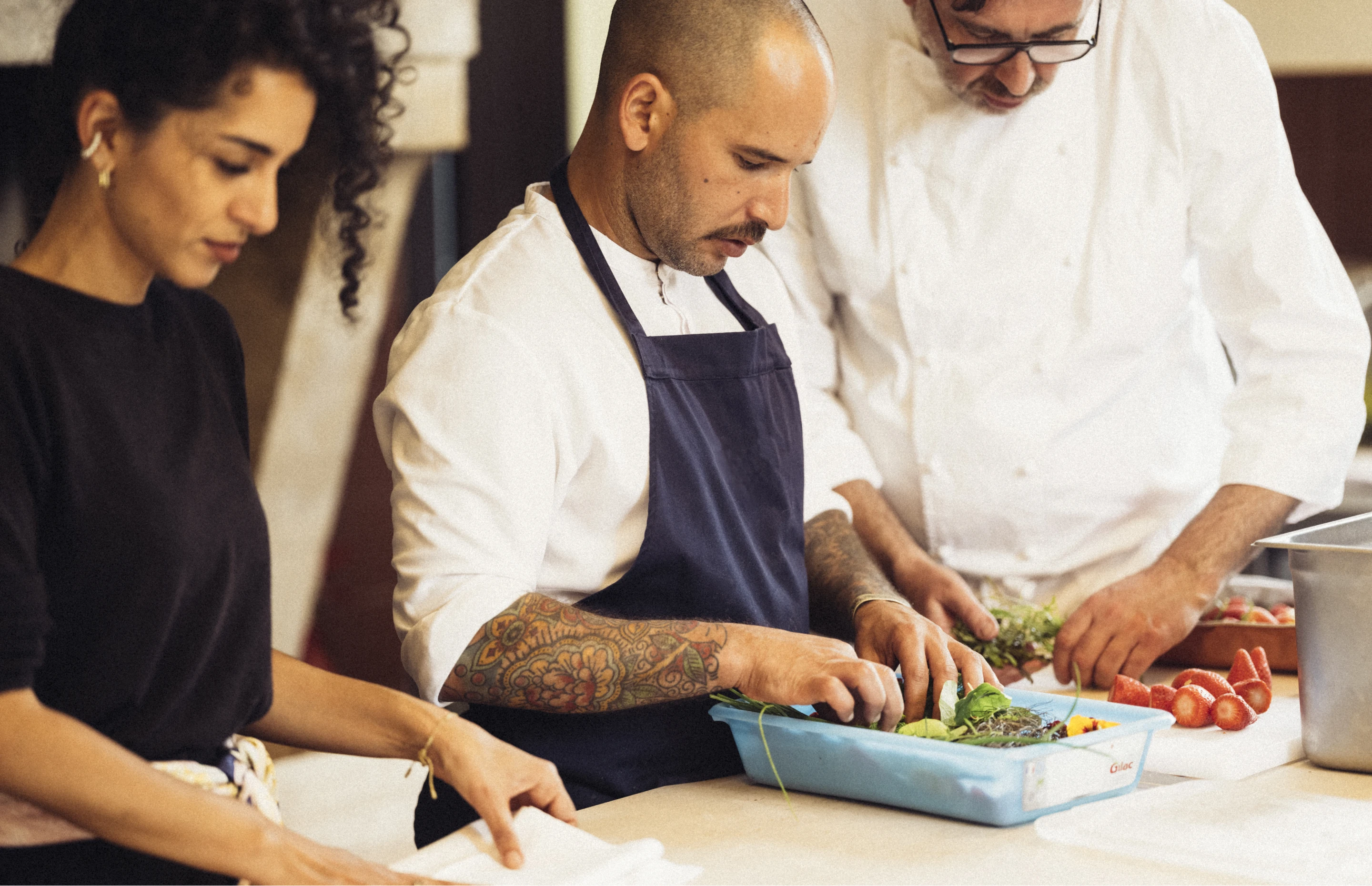 Trois personnes préparant des ingrédients frais ensemble dans une cuisine professionnelle.