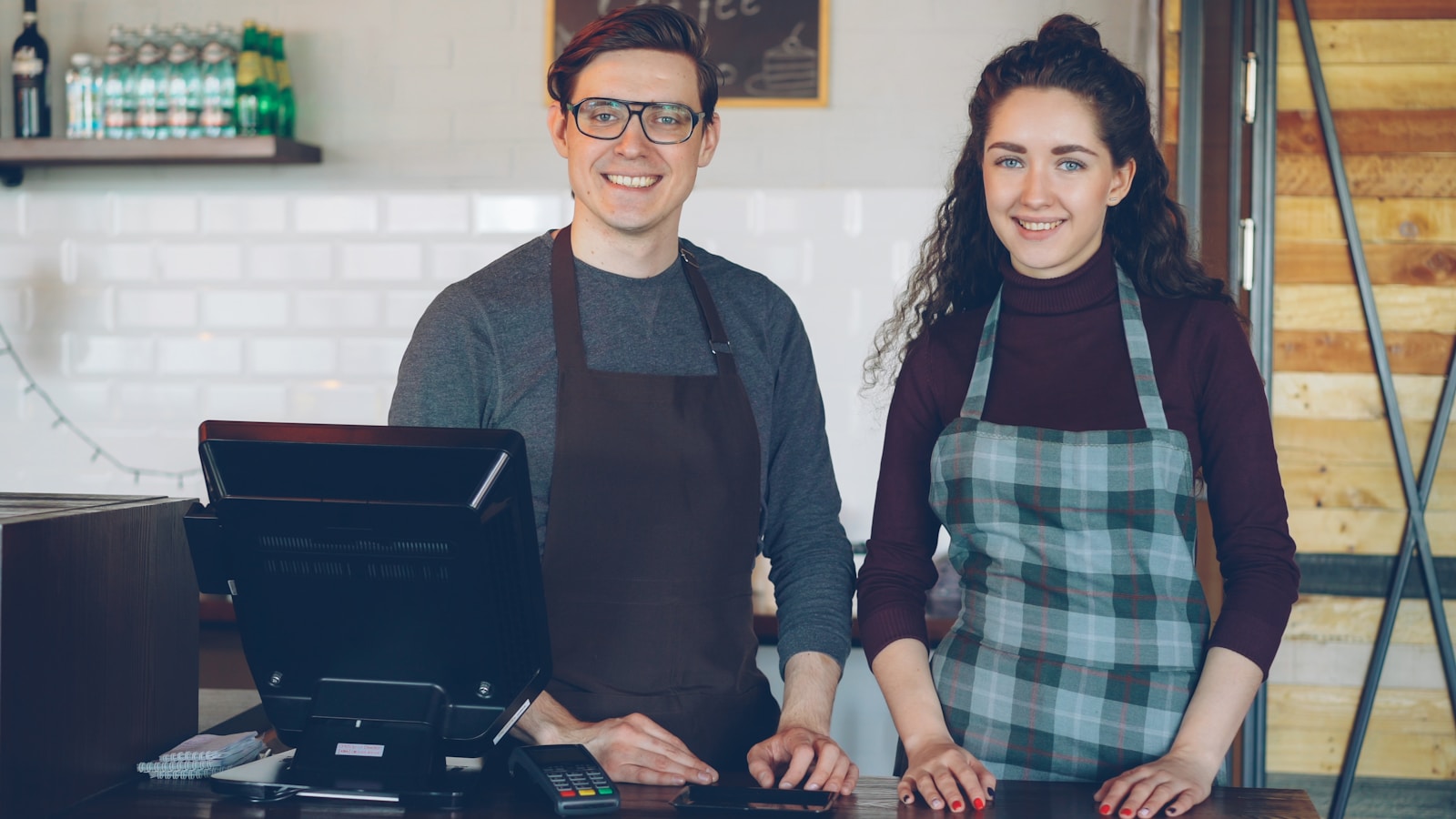 Deux baristas souriants prêts à servir derrière le comptoir de leur café, ambiance accueillante et préparée (photo Vitaly Gariev via Unsplash)