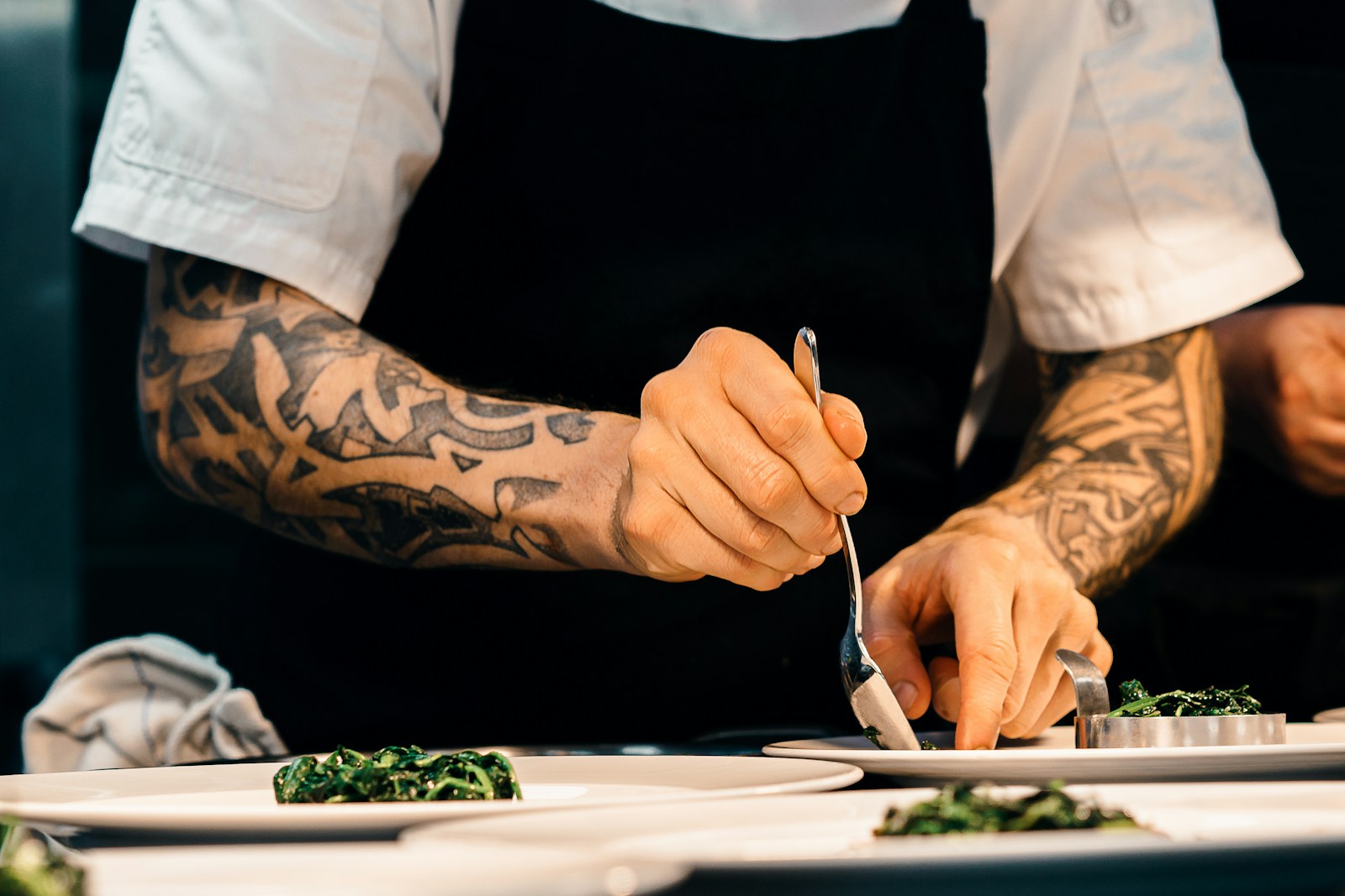 Un cuisinier dresse soigneusement un plat sur une assiette dans la cuisine d'un restaurant, la précision du geste rappelle l'attention que demande aussi le détail de chaque plat dans le menu sur la fiche Google (photo Sebastian Coman Photography via Unsplash)