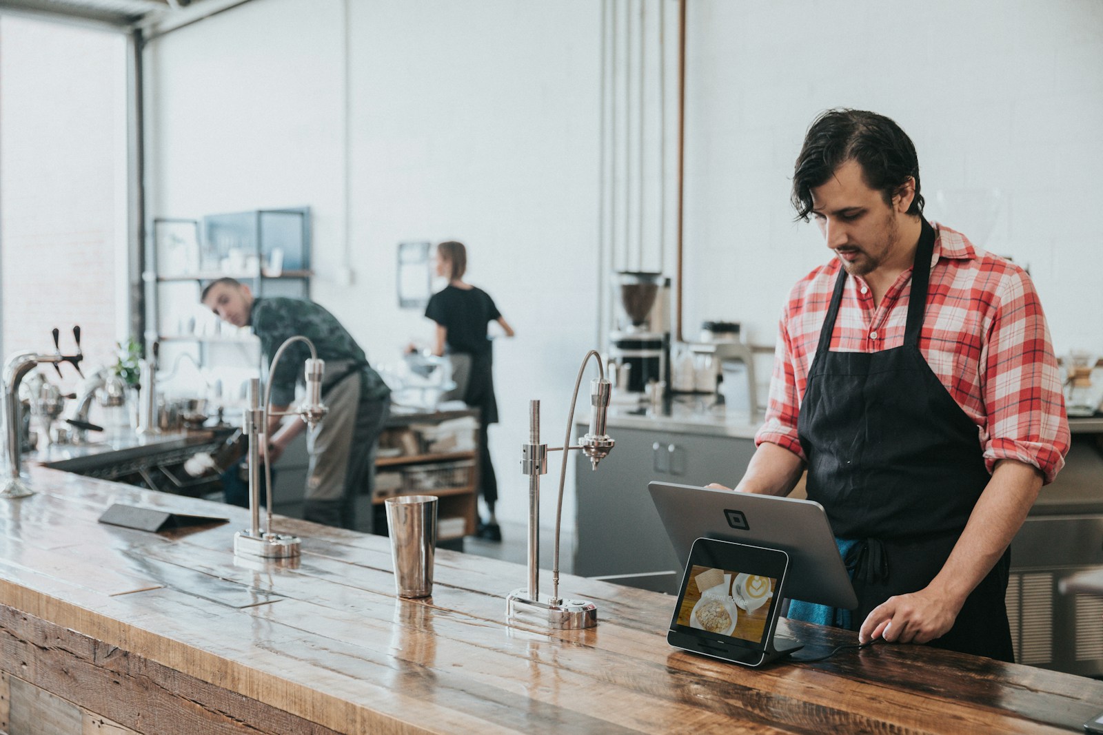 Un restaurateur en tablier consulte une tablette au comptoir de son établissement, prêt à ajuster sa présence en ligne pour la rentrée (photo Nathan Dumlao via Unsplash)