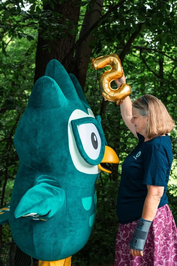 Frau in Lern-Fair T-Shirt vor Wald mit Eulen Maskottchen