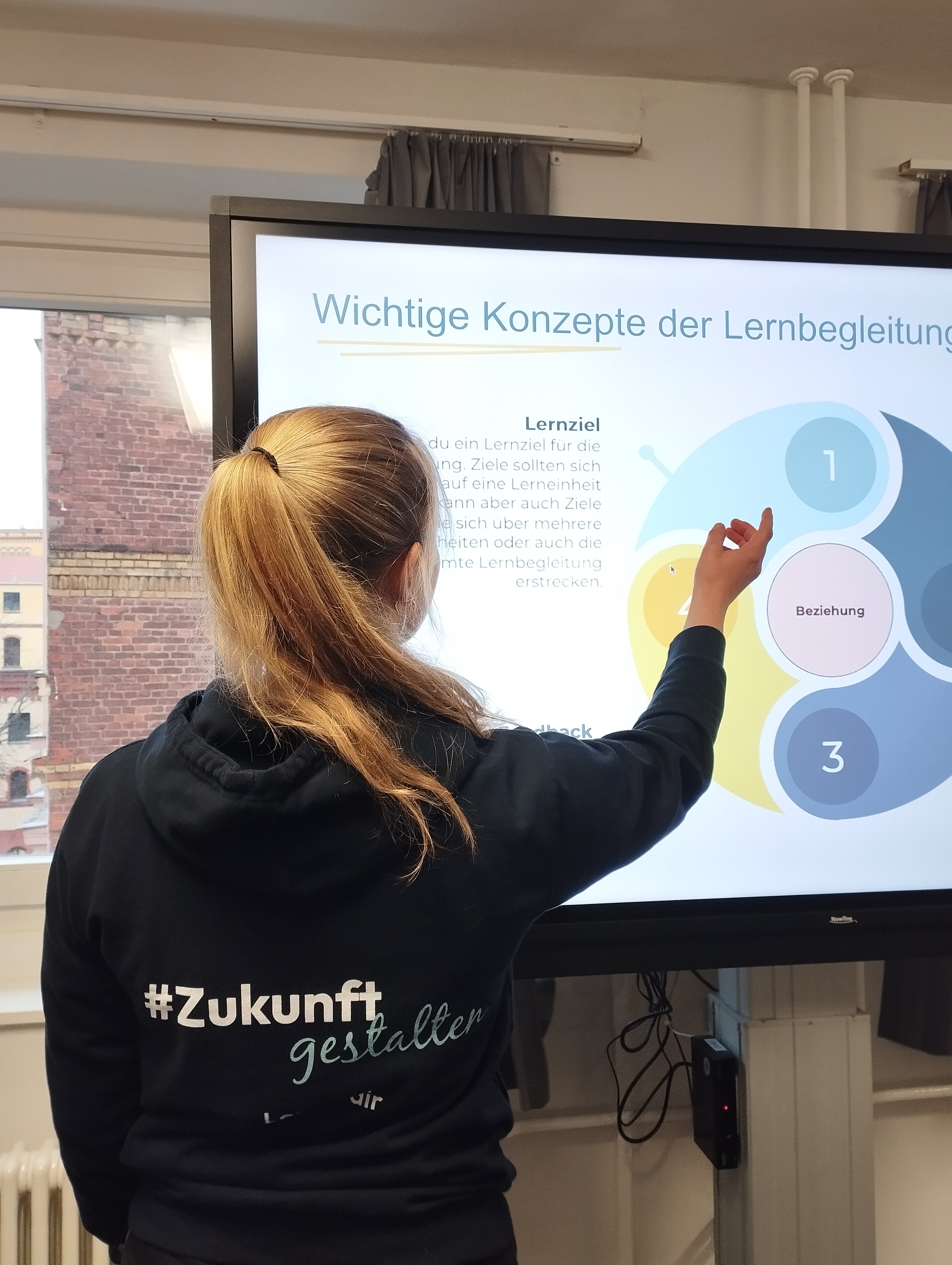 Junge Frau mit Rücken zur Kamera zeigt auf Präsentation