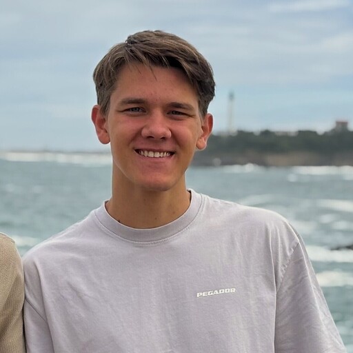 Junger Mann lächelt in die Kamera. Im Hintergund ist Wasser.