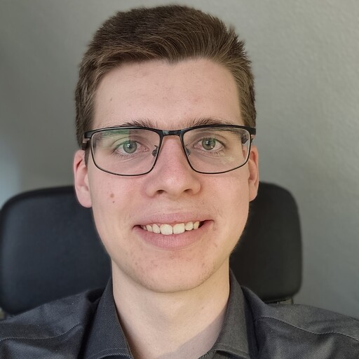 Ehrenamtliches Team-Mitglied sitzt am Schreibtisch und lächelt in die Kamera seines Computers.