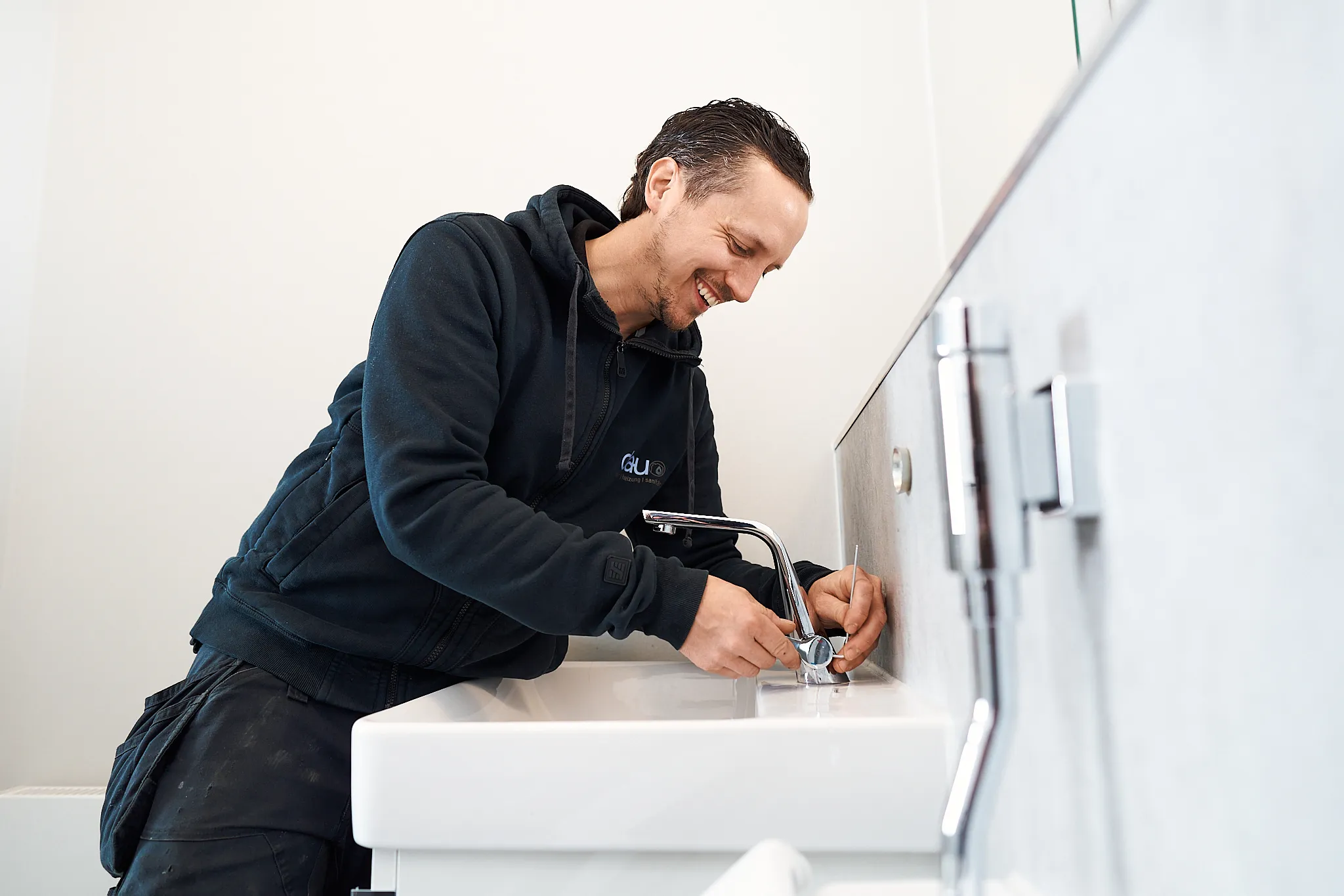 Techniker repariert lächelnd einen Wasserhahn eines weißen Waschbeckens im Badezimmer.