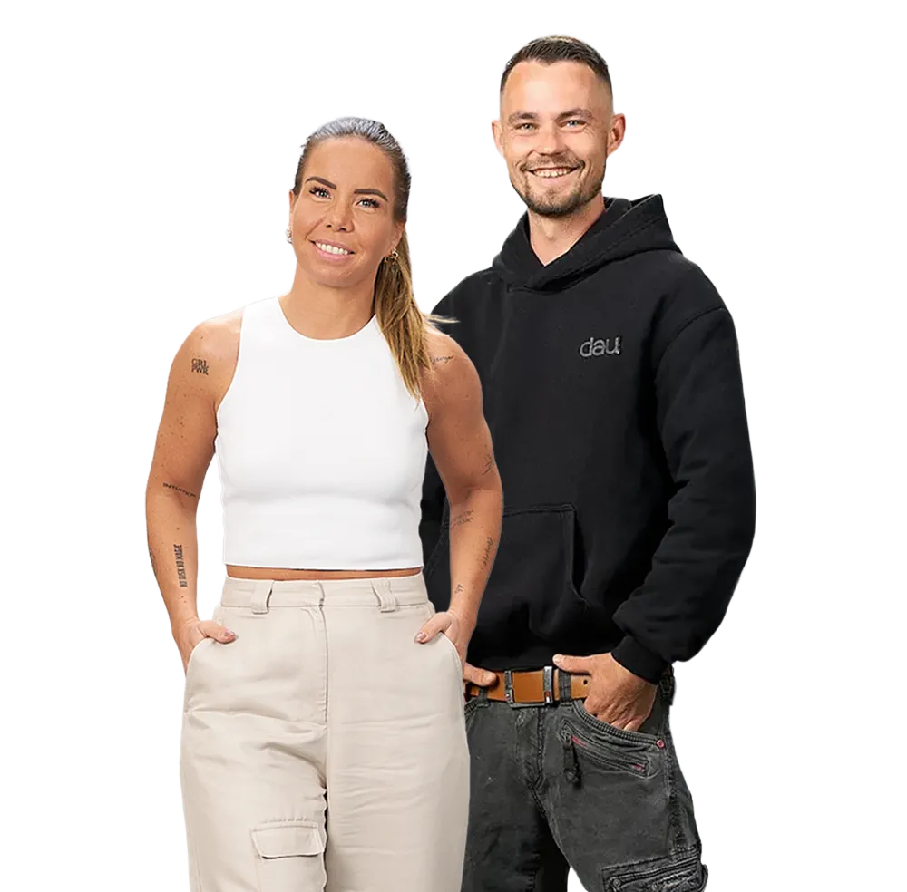 Frau mit weißem Top und hellen Hosen neben Mann mit schwarzem Hoodie und dunklen Hosen, beide lächeln.