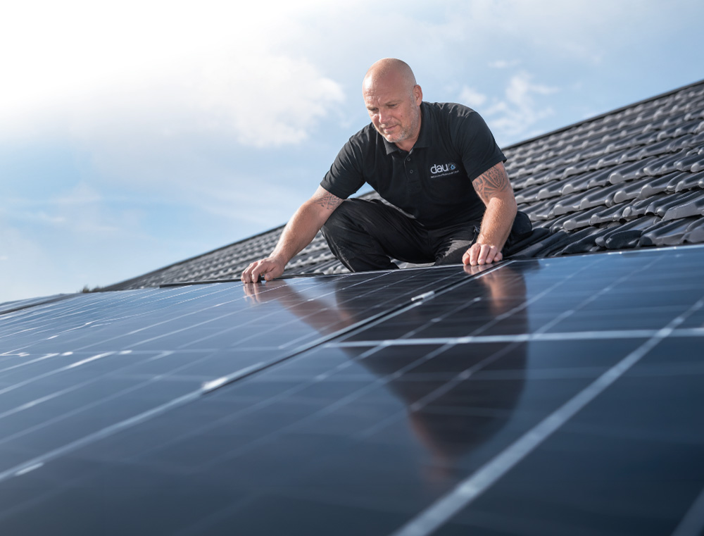 Zwei Männer installieren Solarpaneele auf einem schrägen Dach bei bewölktem Himmel.